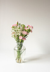 Vertical closeup of pink carnations and white gypsophila baby's breath in glass vase (selective focus)