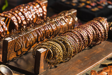 Selective focus forged metal wrist bracelets handmade by a blacksmith on an artisan counter glisten in sunlight on a wooden stand