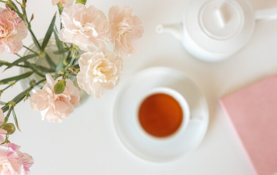 Close up of soft pink carnations from above with tea cup, journal and tea pot in background (selective focus) - Powered by Adobe