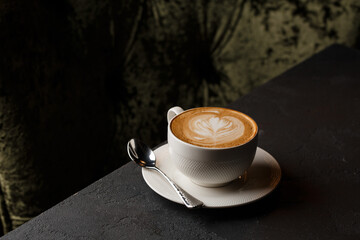 White cup of hot latte coffee with beautiful milk foam latte art texture isolated on dark...