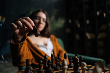 Selective focus of cute businesswoman in elegant eyeglasses making chess move sitting on armchair...