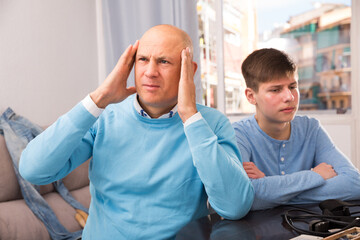 Portrait of offended father after quarrel with son sitting at home