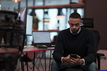 Young African American work in coworking space using smartphone analyzing online market trends, focused man worker reading financial news or browsing internet on phone. Technology concept