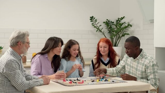 Multi Ethnic family of different age generations play board game at home sitting at the table. The African American dad throws the dice on the table and loses. Family Meeting, Different Generations.