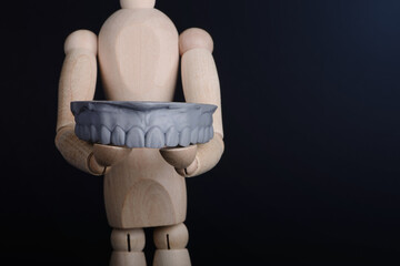 Human wooden figure holds in hands a dental upper jaw model printed on 3d printer on a black background. © gorynvd