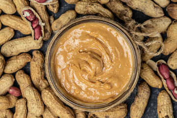 peanut paste in an open jar. creamy peanut butter peanuts scattered. top view