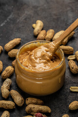 Peanut butter in glass jar and spoon on dark background, American dessert concept. vertical image. top view. place for text