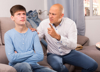 Portrait of angry man scolding teenage son in living room at home