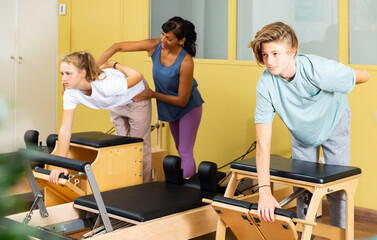 Young boy and girl doing pilates exercises during group training. Hispanic woman trainer teaching them.