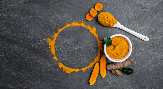 turmeric powder in spoon with turmeric root. curcuma or curcumin on concrete background. Spice, natural coloring, alternative medicine. Long banner format. top view