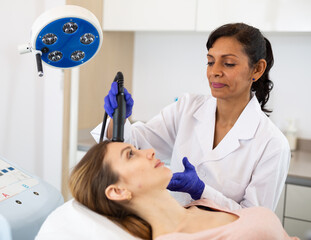 Hispanic woman beautician using equipment for needle-free mesotherapy for her patient, young...