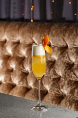 Glass of a delicious yellow cocktail French 75 standing on the bar counter on the blurred dark and yellow light background