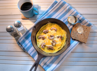 Top View of cooked mushroom and cheese omelette in cast iron skillet on white natural wood table