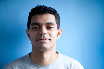 Man with optimistic and hopeful smile looking at cameraBrazilian boy looking at camera on blue background. People concept. Man concept.