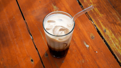 Iced cappuccino in tall clear glass served on a brown wooden table