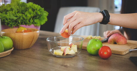 Obraz na płótnie Canvas Woman cutting apple on wooden board, preparing fruit salad in the kitchen..