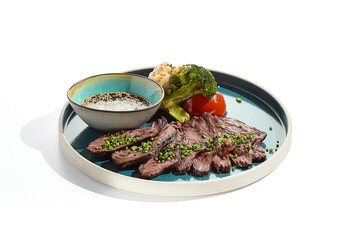 Roast beef with vegetables and sauce on trendy plate. Sliced meat steak roast grill with tomatoes and broccoli isolated on white table. Angus roast beef in healthy style for restaurant.