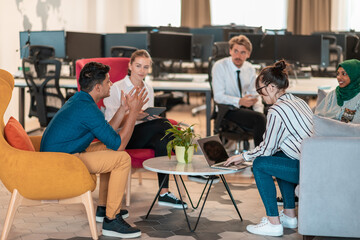 Multiethnic startup business team having brainstorming in relaxation area of modern office interior working on laptop and tablet computer