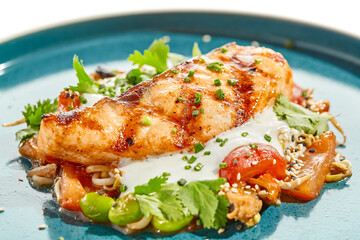 Healthy food - baked salmon steak with tomato salad and white sauce. Roast salmon with vegetables on contemporary plate in asian style. Restaurant dish - salmon filet with hard shadow.