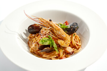 Italian dish - seafood linguine isolated on white background. Pasta with prawn, mussels, octopus,  squid in tomatoes marinara sauce. Seafood pasta in Italian restaurant menu. Seafood on white plate