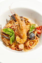 Italian dish - seafood linguine isolated on white background. Pasta with prawn, mussels, octopus,  squid in tomatoes marinara sauce. Seafood pasta in Italian restaurant menu. Seafood on white plate