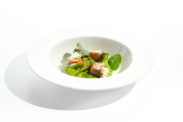 Gourmet food - green risotto with broccoli and salmon on white background. Italian lunch with risotto and sliced grilled salmon. Contemporary dish for restaurant menu. Hard shadow in sunshine day.