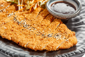 Authentic German schnitzel with cabbage salat and sauce on black plate. Breaded meat - popular restaurant dish Viennese schnitzel. Thin slice of meat breaded with vegetables salad on white background.