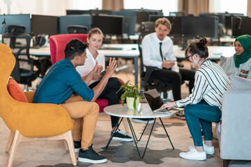 Multiethnic startup business team having brainstorming in relaxation area of modern office interior working on laptop and tablet computer