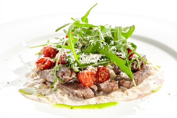 Meat medallions with mushroom creamy sauce and rucola salad on white background. Meat steak on mushroom gravy with tomato and rocket salad. Roasted beef fillet with vegetables salad in restaurant.