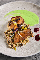 Roasted beef tongue with green buckwheat and green sauce. Main course with beef tongue and garnish on gray stone table. Aesthetic composition with meat dish and textile. Beef in restaurant menu.