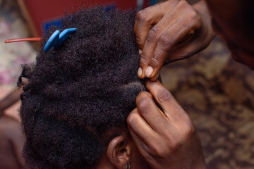 Hands of an african Nigerian hair dresser or stylist making weaving hairstyle for a client in saloon