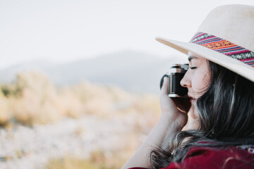 Close up of young latin woman wearing a red poncho and a hat, taking photos with a vintage camera.