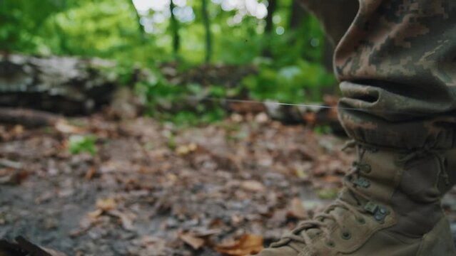 Close up soldier male legs in army boots walk on the ground in camouflage uniform. In forest near tree