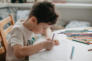 The boy draws with pencils at the kitchen