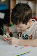 The boy draws with pencils at the kitchen