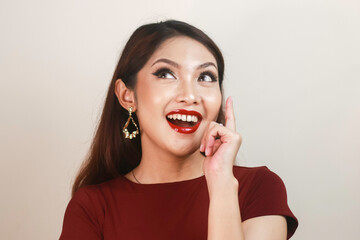 Shock face of a young Asian woman wearing a red shirt pointing upwards. Advertisement concept.