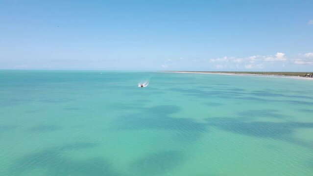 Wide angle drone shot approaching a boat going past the frame driving on the crystal clear blue waters off the coast of the tropical island of Holbox in Mexico shot in 4k.