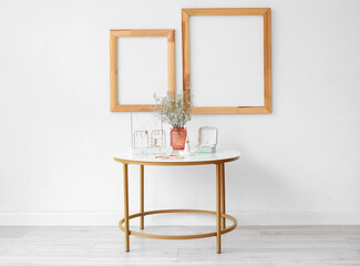 Stylish jewelry, vase with flowers on table and blank frames in room
