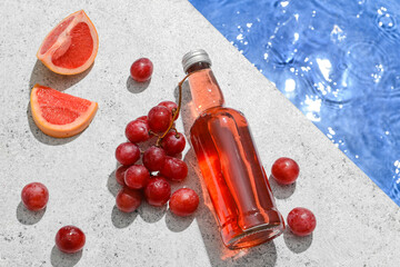 Bottle of tasty soda with grape and grapefruit near swimming pool