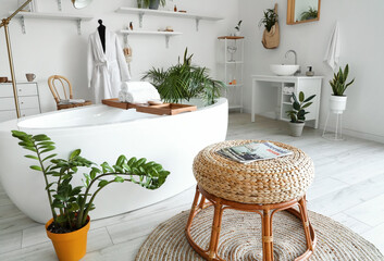 Interior of light bathroom with bathtub, mannequin and houseplants