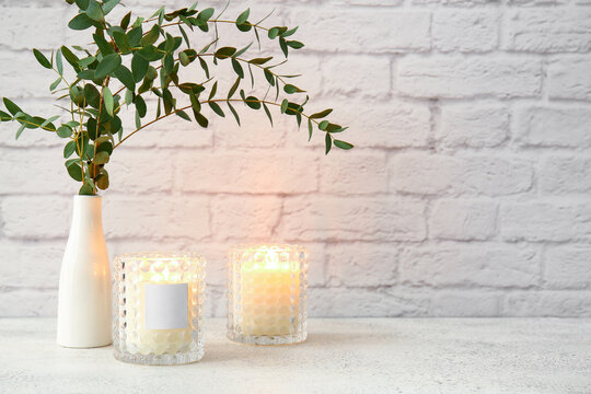 Glass holders with burning candles and eucalyptus branches on light table
