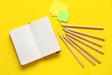 Blank notebook and colorful pencils on yellow background
