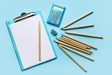 Clipboard with blank paper sheet, sharpener and colorful pencils on blue background