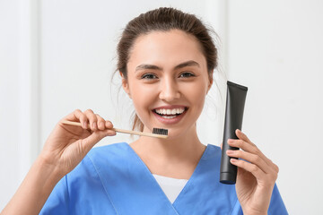 Female dentist with activated charcoal tooth paste and brush on light background