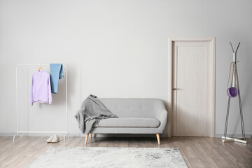 Rack with clothes, sneakers and sofa near light wall