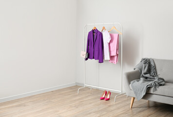 Rack with clothes, heels and sofa near light wall