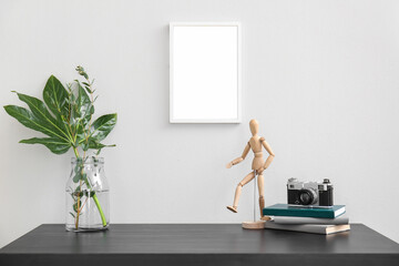 Workplace with plant branches in vase, wooden mannequin, notebooks and photo camera near light wall