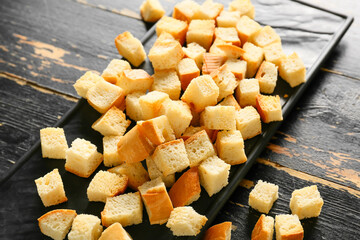 Board with tasty croutons on dark wooden background, closeup