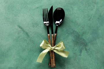 Cutlery with ribbon on green background, top view