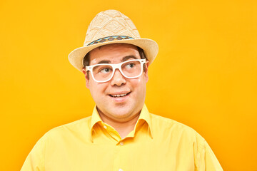 Positive man in panama hat thinks about vacation, doubts, makes decision isolated on yellow studio background